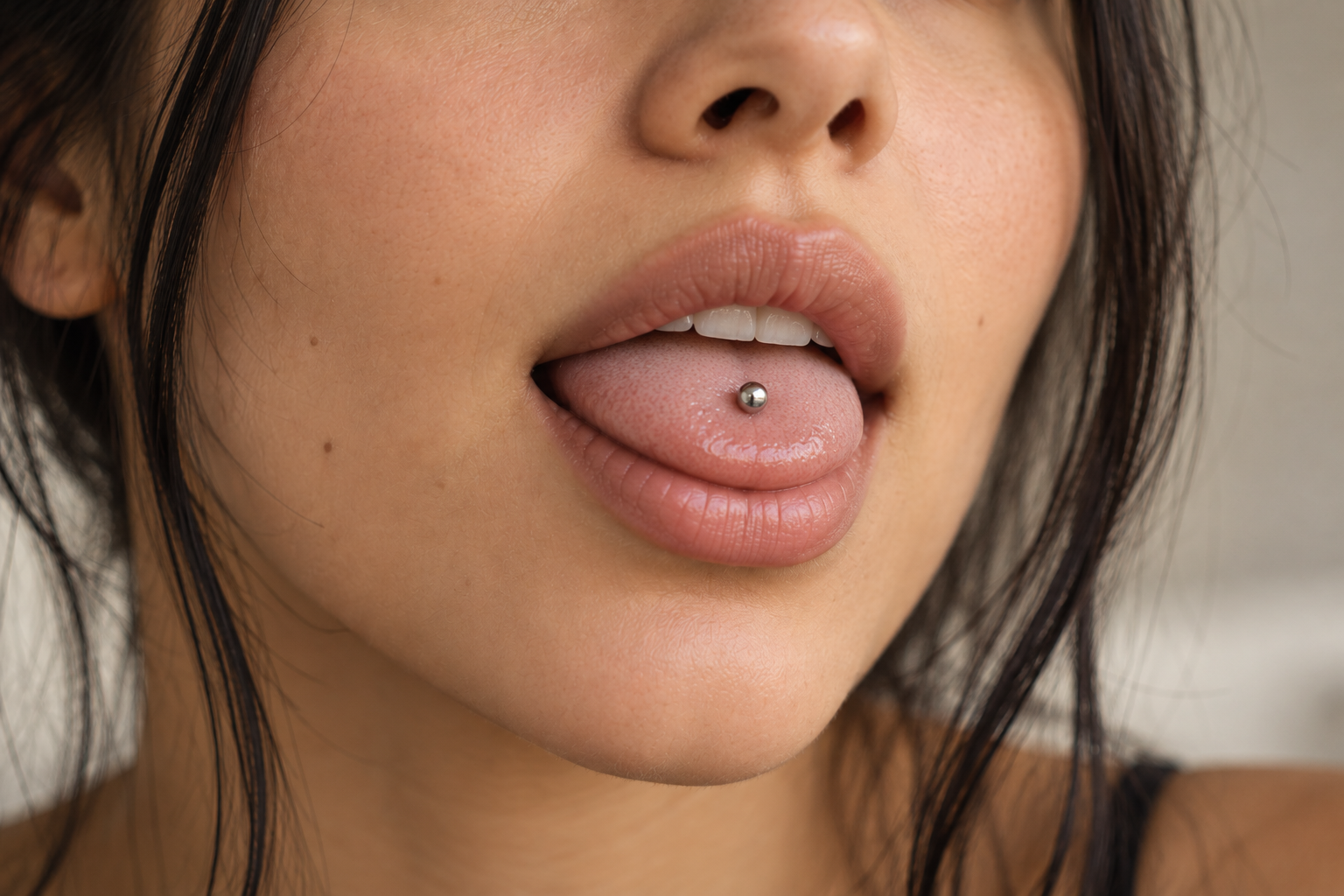 Woman with a healed midline tongue piercing: a single silver ball in the center of her tongue