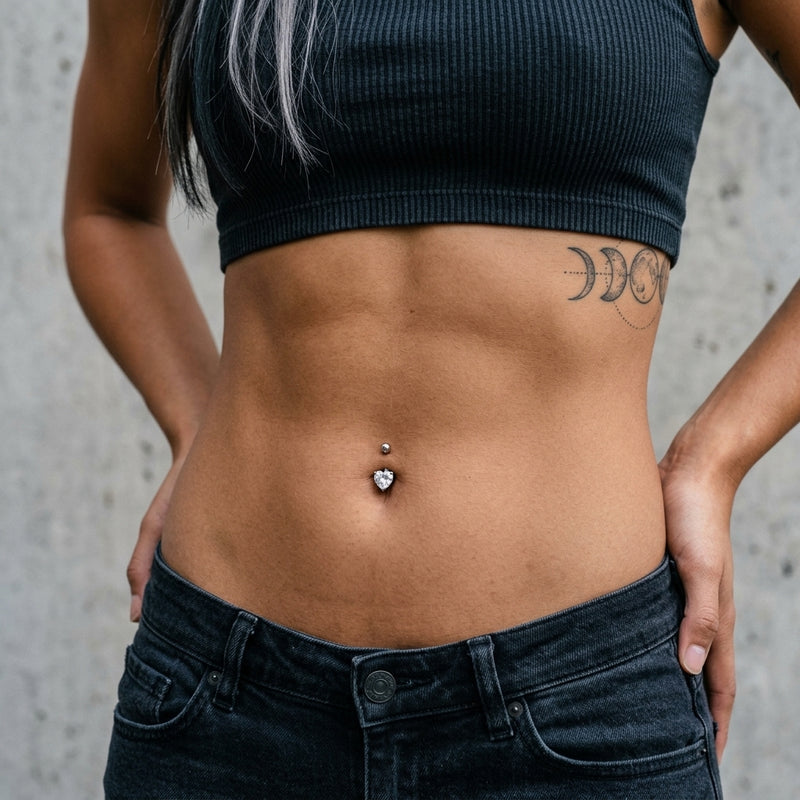 14G surgical steel belly ring with heart-shaped clear CZ gem, shown worn in a navel piercing