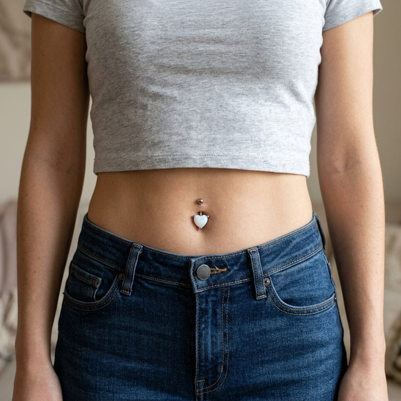 14G surgical steel navel ring with a white glitter opal heart gem, worn in a navel piercing