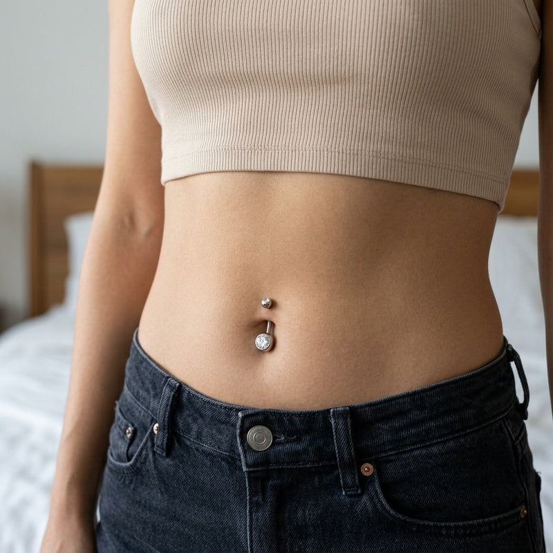 14G titanium curved navel ring with clear CZ gem balls, shown worn in a navel piercing