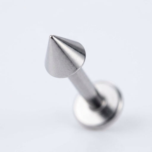 16G titanium labret stud with a sharp cone spike end and flat back, close-up angled view on a white background