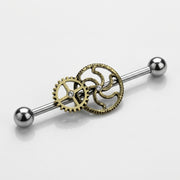 14G surgical steel industrial barbell with ball ends and brass steampunk gears with clear CZ gems, three-quarter view